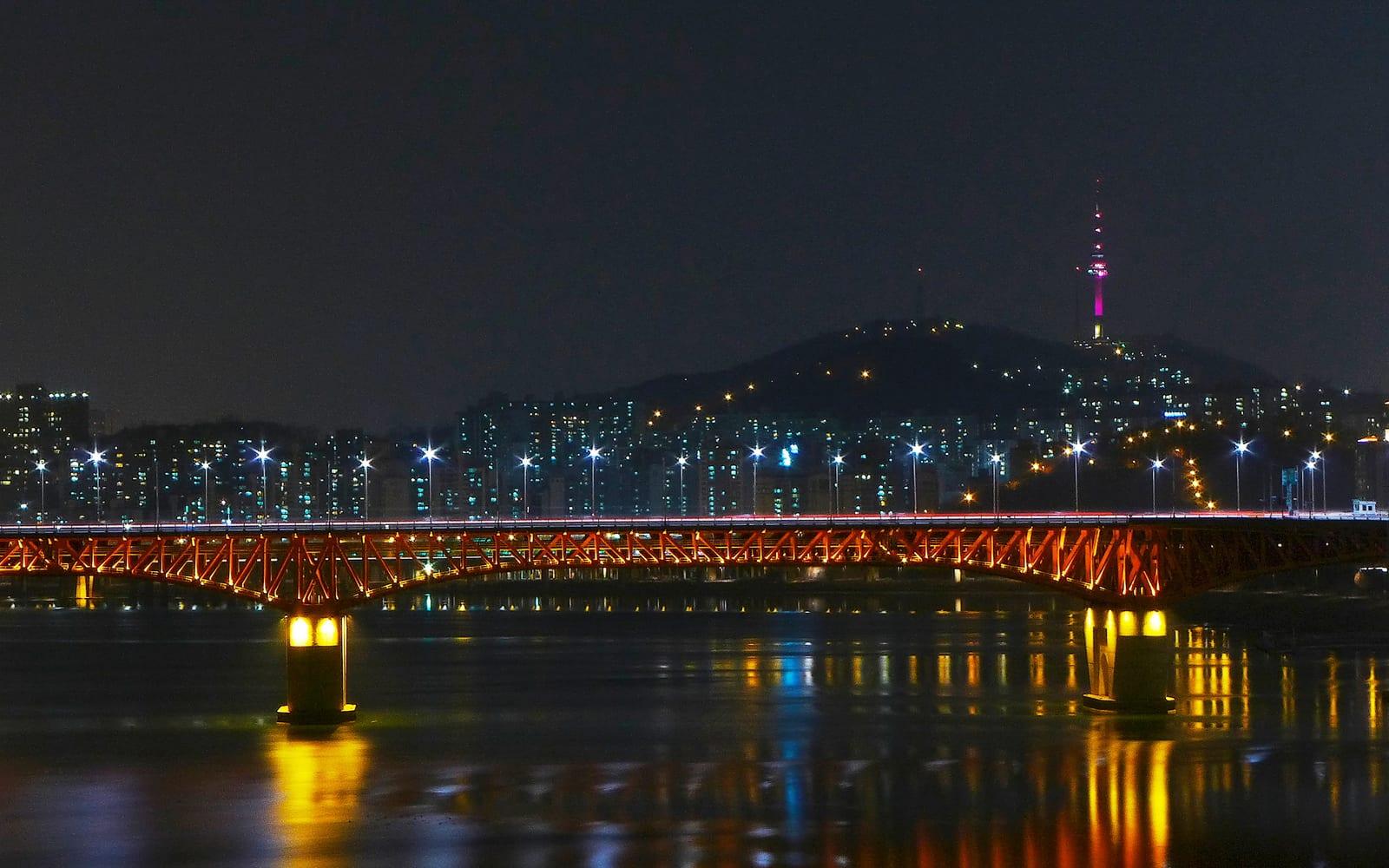 밤의 한강을 가로지르는 붉은 성수대교. 능선 위로 남산서울타워가 서 있습니다.